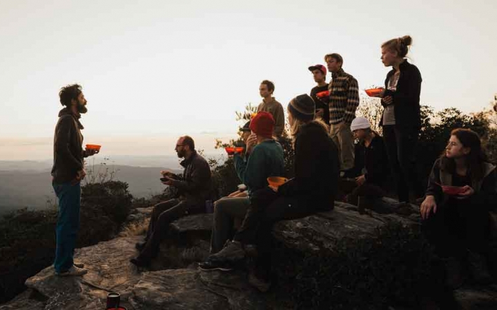 an instructor speaks to a group of students while they eat breakfast on a backpacking trip in north carolina